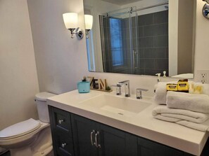 Ein Badezimmer mit weißem Waschbecken, dunklen Schränken, einer Toilette und einer Dusche mit Glastür.