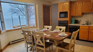Una cocina con armarios de madera, una mesa de comedor preparada para seis comensales, y un amplio ventanal con vistas al agua.