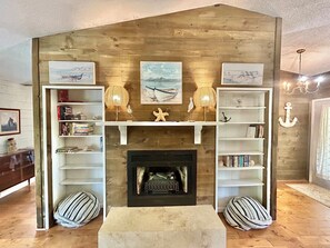 A cozy living room with a fireplace, wooden shelves, and decorative items. - Our Anchor - close to the beach! (St. George Island)