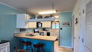 Uma cozinha compacta com ilha central, banquetas de bar e uma mesa de jantar com toalha de mesa florida.