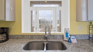 A kitchen with a double sink, granite countertop, and a window above the sink. - See Escape-Beachfront, Pet Friendly, Hot Tub 4BR (St. George Island)