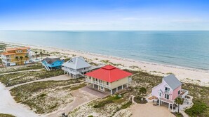 A coastal property with multiple buildings, including a large house with a red roof and a smaller blue house, both with white balconies and a beach view. - See Escape-Beachfront, Pet Friendly, Hot Tub 4BR (St. George Island)