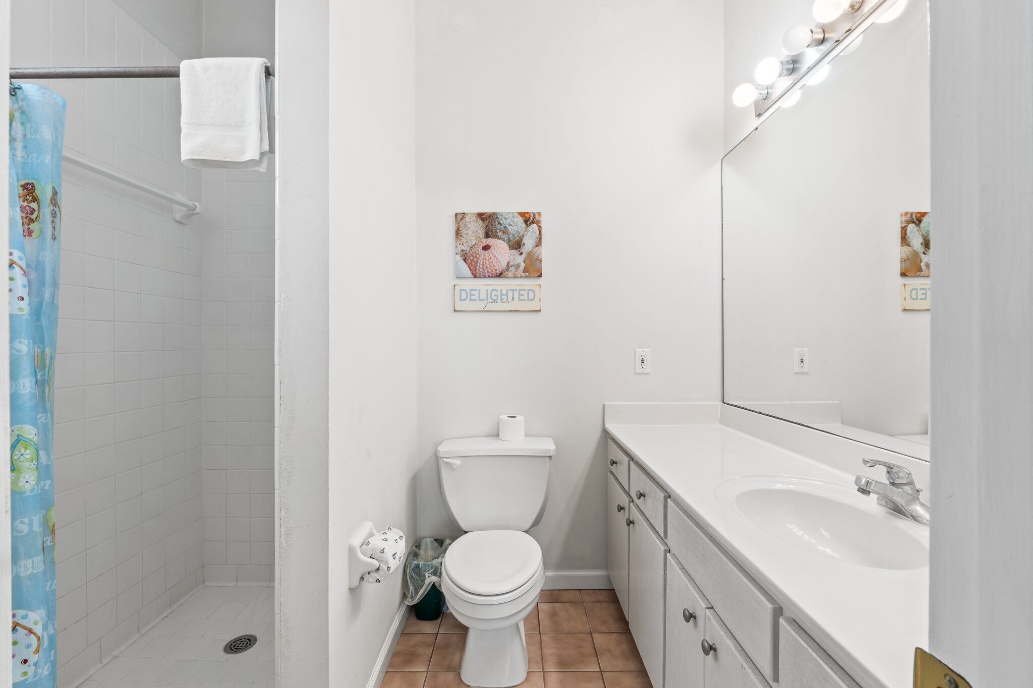 A bathroom with a shower, toilet, sink, and a mirror with lights.