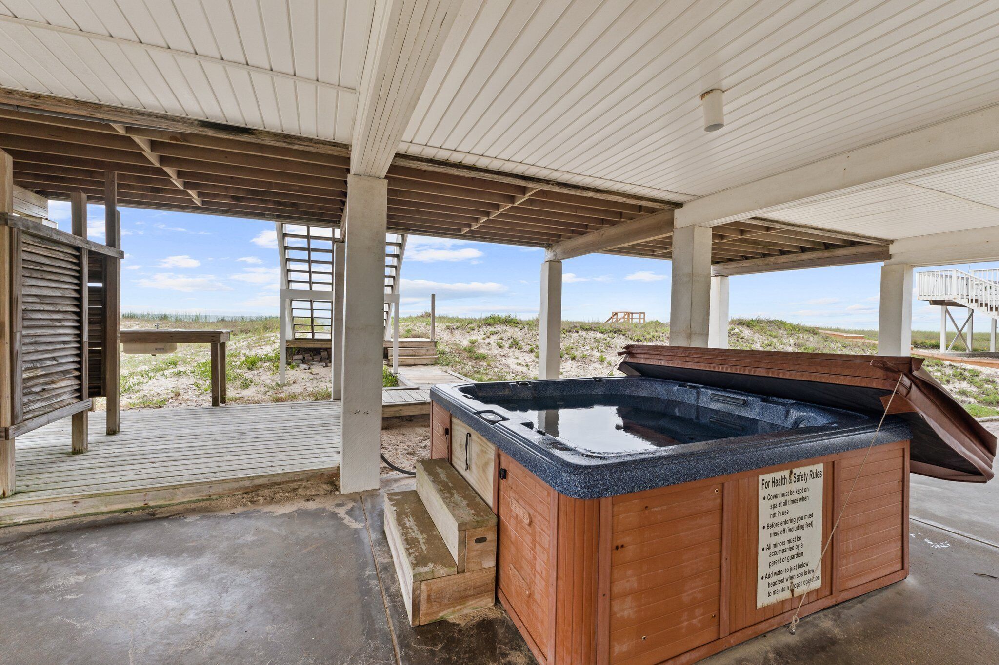 A wooden hot tub under a covered area with a view of the beach.