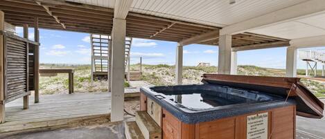 A wooden hot tub under a covered area with a view of the beach.