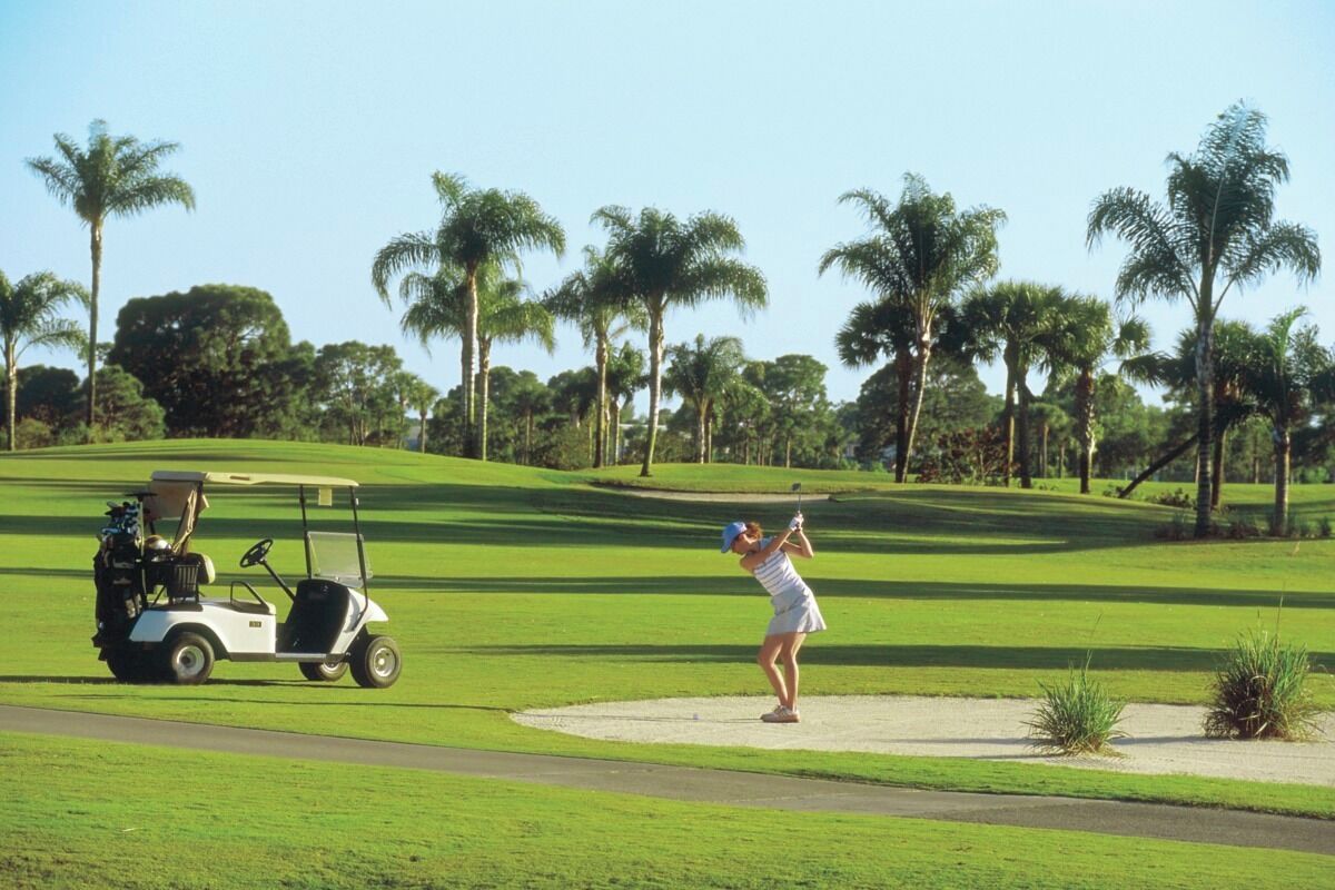 Ein Golfplatz mit einem Golfer in weißer Kleidung und einem Golfwagen.
