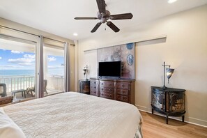 Ein Schlafzimmer mit einem großen Bett, einem Deckenventilator, einem Fernseher und einem Balkon mit Meerblick.