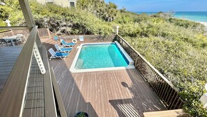 Una terraza de madera con piscina, sillas de descanso y vista al océano.