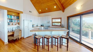 Una cocina moderna con armarios blancos, una isla central con taburetes de bar, un refrigerador y un amplio ventanal con vistas al exterior.