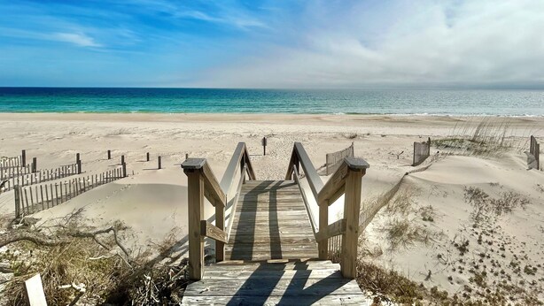 Un paseo marítimo de madera que conduce a una playa con vista despejada al océano.