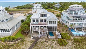 A large, multi-story beachfront property with a pool, multiple decks, and a view of the ocean.