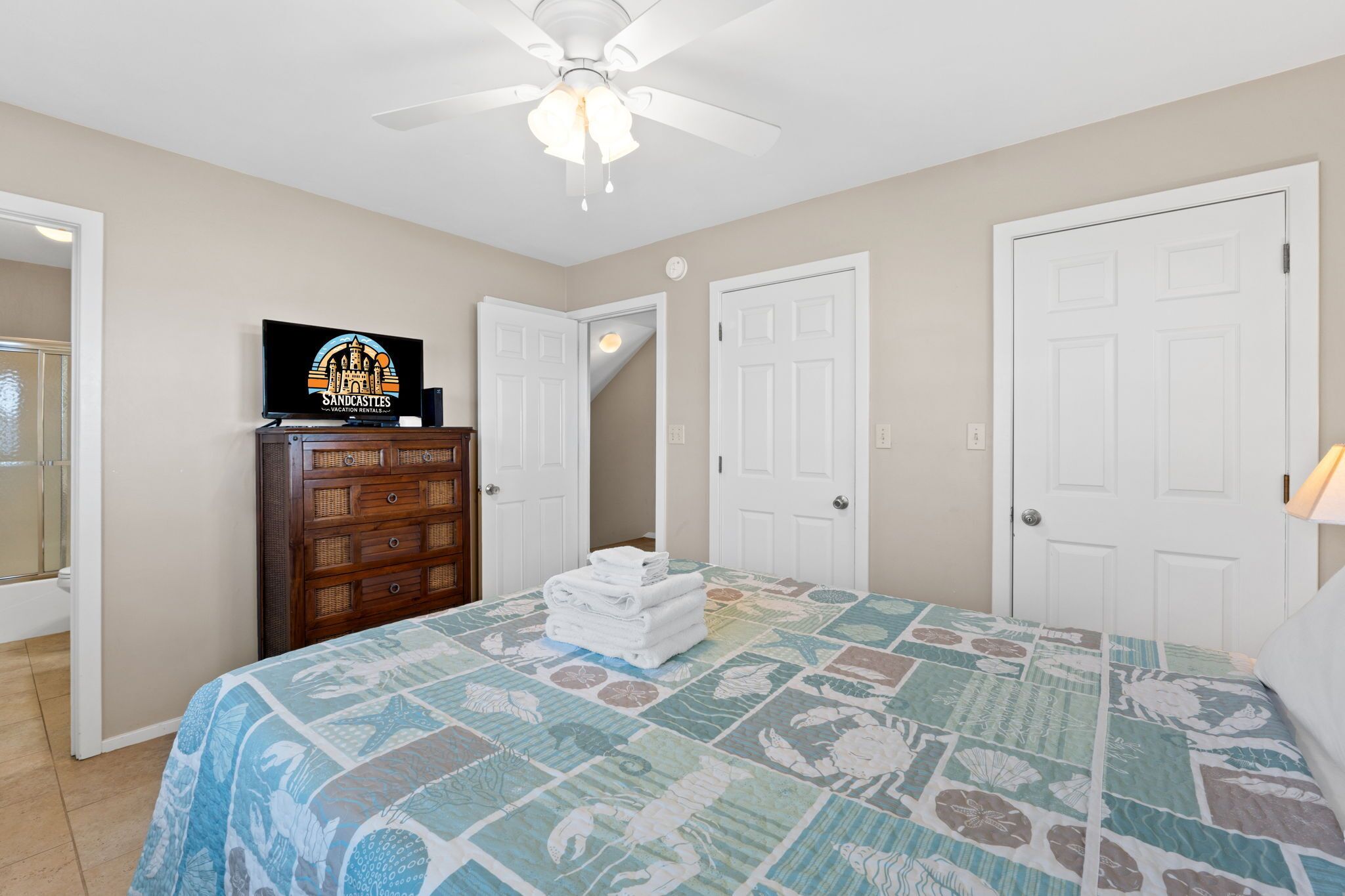 A bedroom with a bed, a dresser, a ceiling fan, and a TV on the dresser.