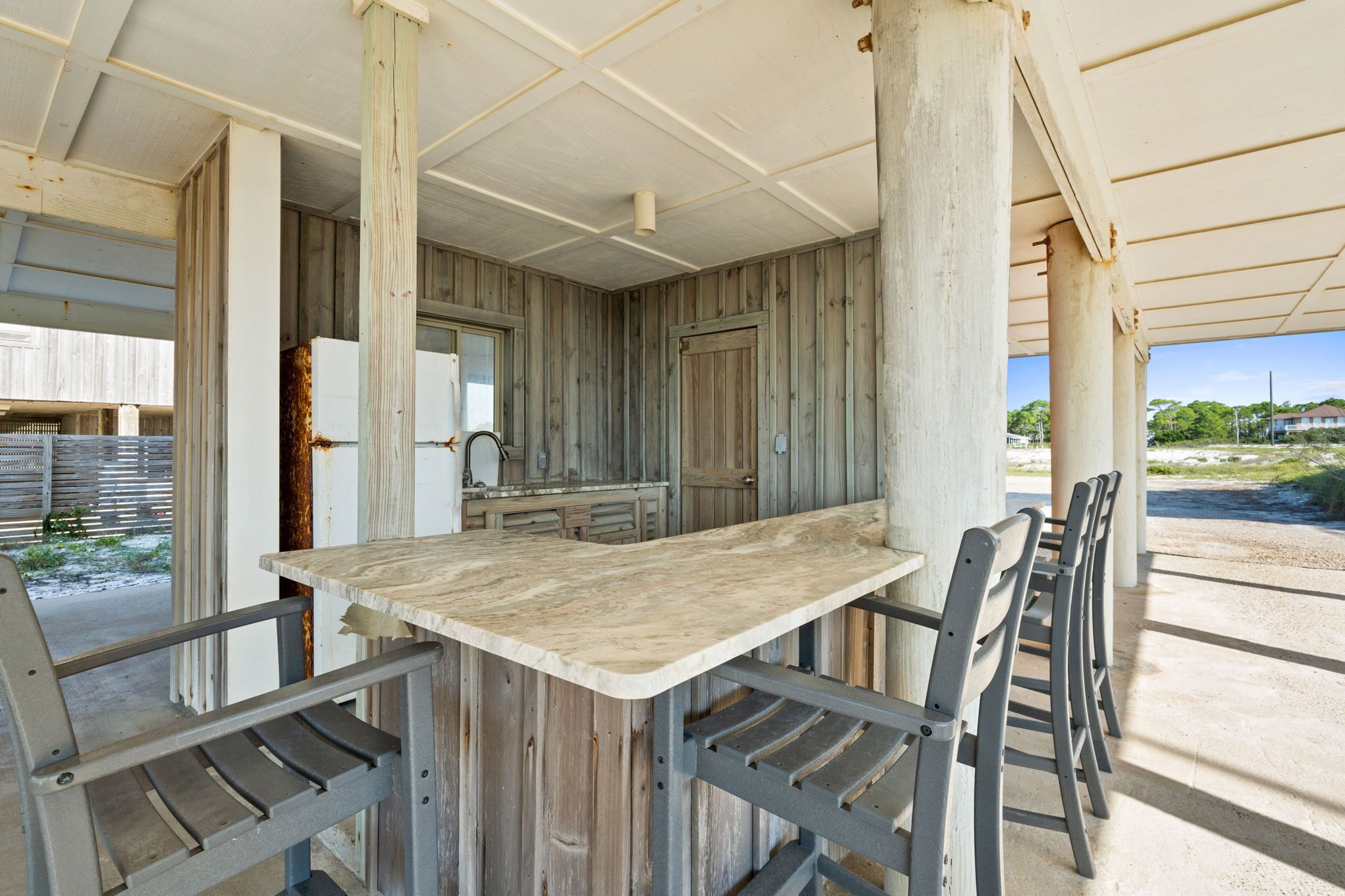 Un comedor al aire libre rústico con una mesa de madera y sillas de metal, rodeado de paredes y columnas de madera.