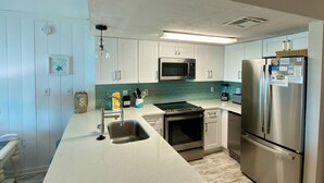 A modern kitchen with white cabinets, a stainless steel refrigerator, a microwave, and an oven. - Ocean Mile F-4, St. George Island, Community Pool, 2 BR (St. George Island)