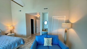 A hotel room with a bed, a blue sofa, a round mirror, a door, and a wall-mounted lamp. - Ocean Mile F-4, St. George Island, Community Pool, 2 BR (St. George Island)