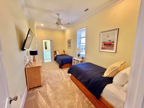 A bedroom with two beds, a ceiling fan, a window, and a door leading to a bathroom. - Southern Splendor, BF, Private Pool, 5BR (St. George Island)