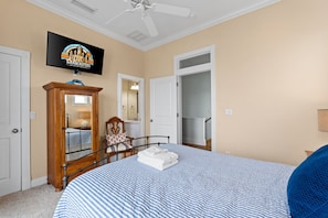 A bedroom with a bed, a wooden wardrobe, a television, and a door leading to a bathroom.