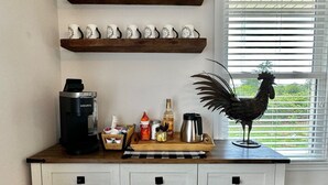 Une cuisine équipée d’une machine à café, décorée d’un coq, et sur laquelle on peut lire l’inscription « Rassemblement » au-dessus d’une étagère remplie de tasses.
