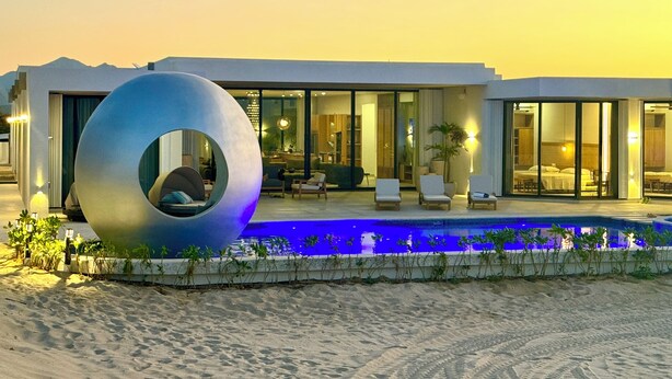 Un hotel modern amb una piscina, una escultura circular gran i un paisatge desèrtic.