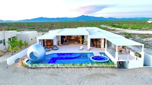 Una casa moderna amb una piscina, una font d'aigua esfèrica i vistes a les muntanyes.