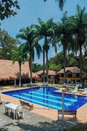 A swimming pool with lounge chairs and tables, surrounded by palm trees and thatched-roof buildings. - La Selva Hotel San Jeronimo (San Jerónimo)