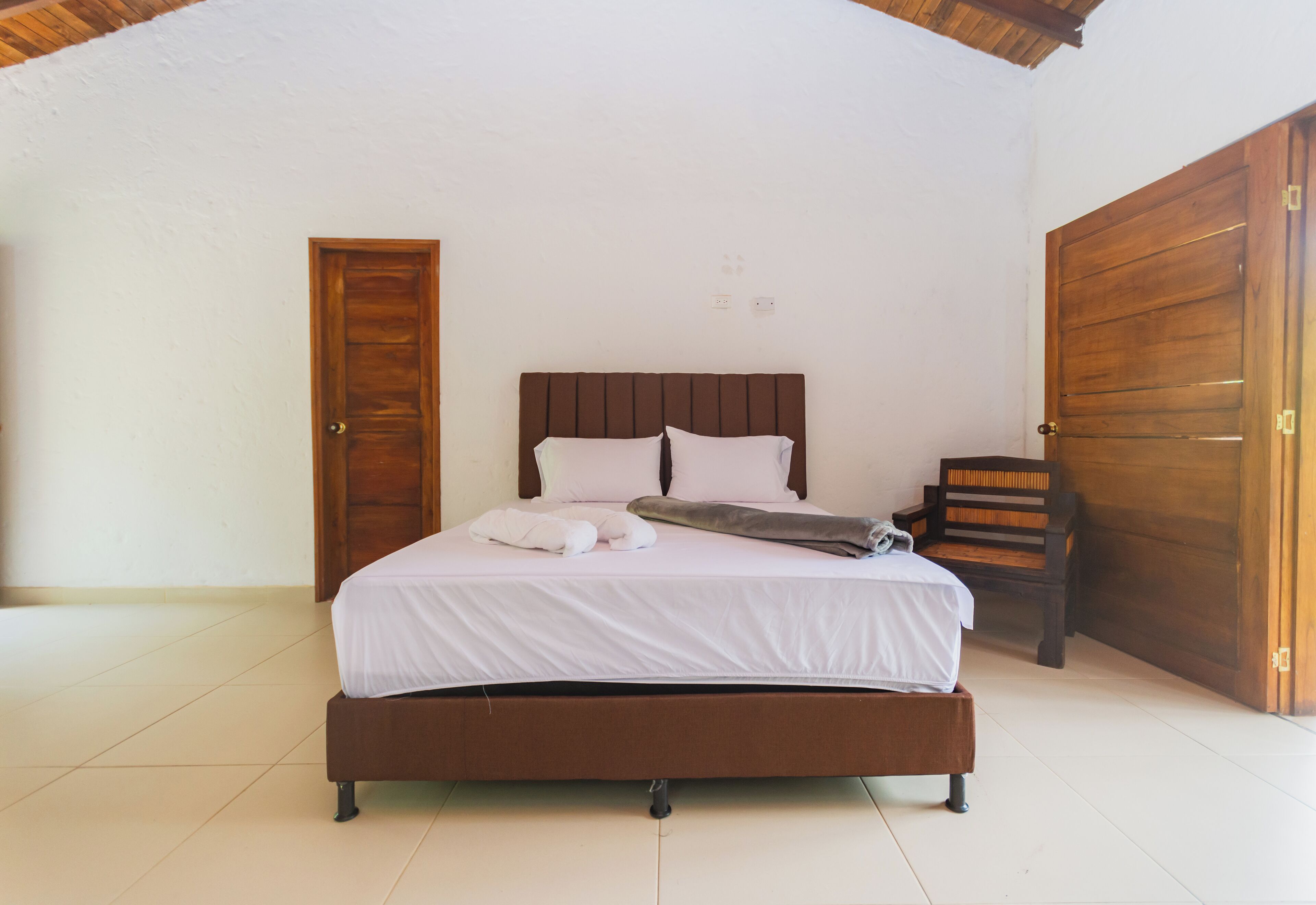 A bedroom with a wooden bed, white bedding, and a bench by the door.