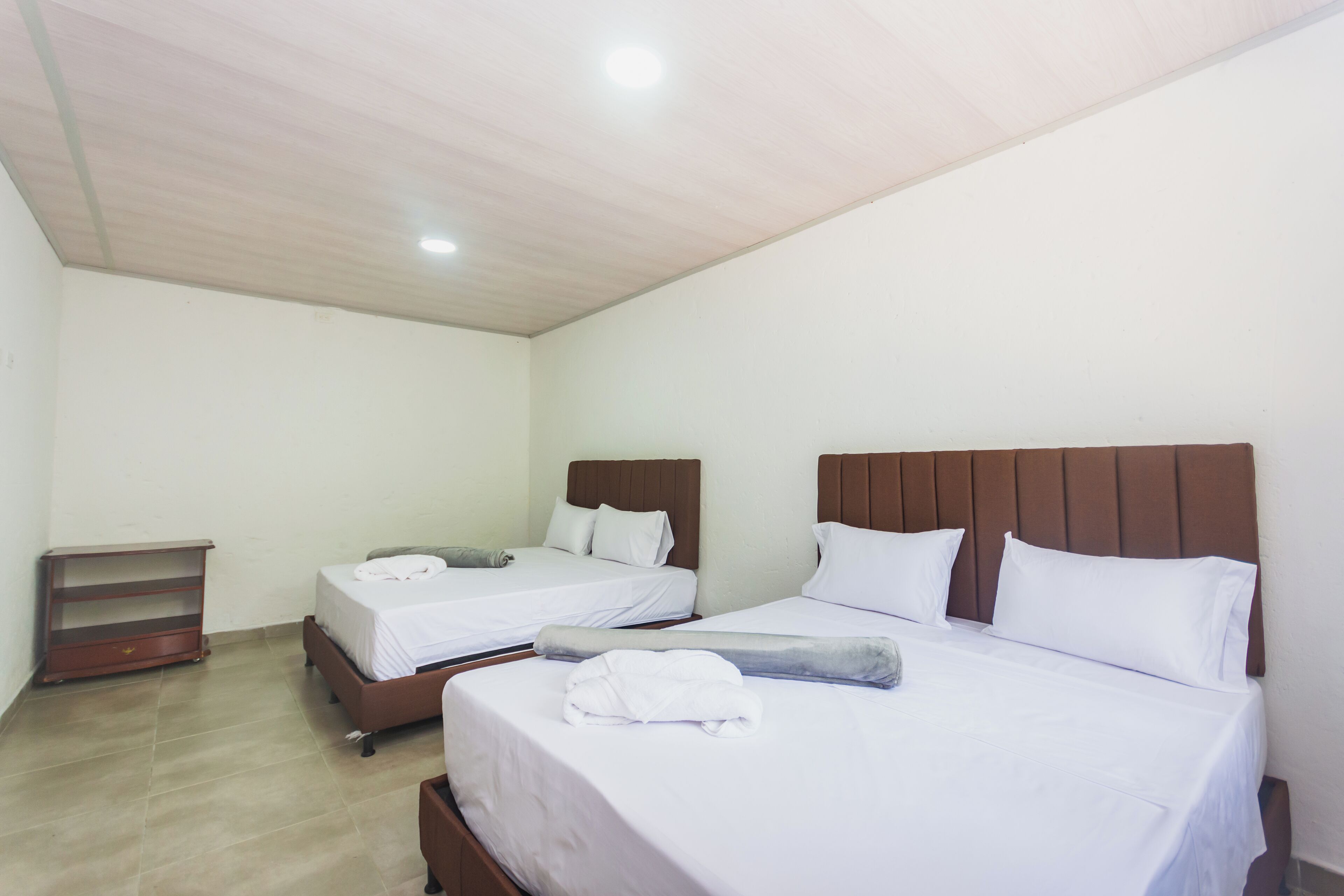 Una habitación de hotel con dos camas, cabeceros de madera, ropa de cama blanca y un pequeño estante de madera.