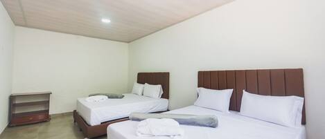 Una habitación de hotel con dos camas, cabeceros de madera, ropa de cama blanca y un pequeño estante de madera.