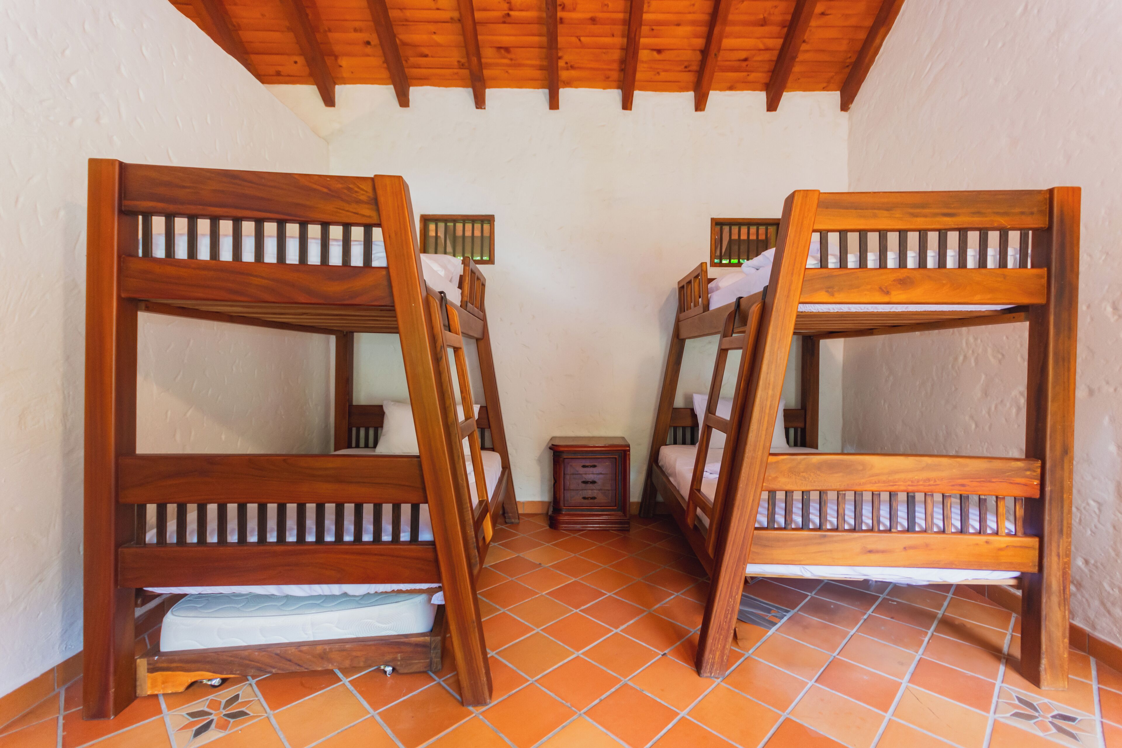 A room with two wooden bunk beds, a small wooden nightstand, and a tiled floor.