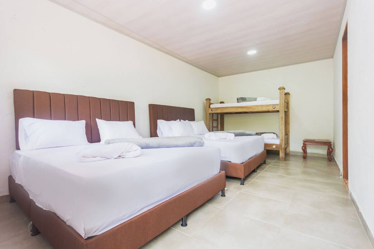 A hotel room with two beds, a wooden bunk bed, and a small wooden table.