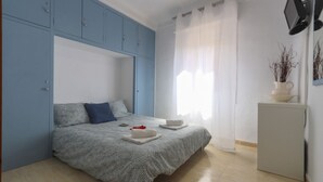 A bedroom with a bed, a small cabinet, a TV, and a window with curtains.