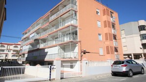A multi-story residential building with balconies, a gated entrance, and a parked car.