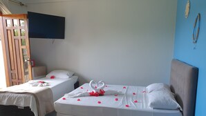 Hotellihuone, jossa on kaksi sänkyä, seinälle asennettu televisio ja koristeellinen seinävaate.