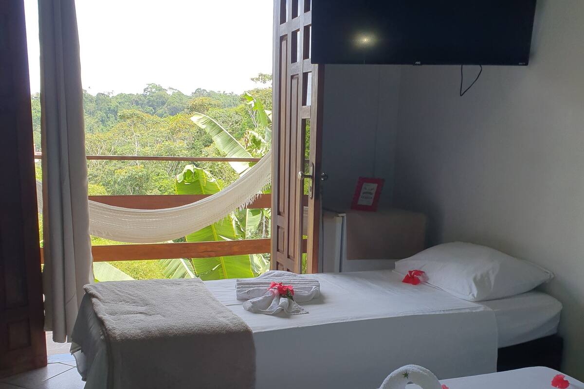 A hotel room with two beds, a hammock, and a balcony with a view of greenery.