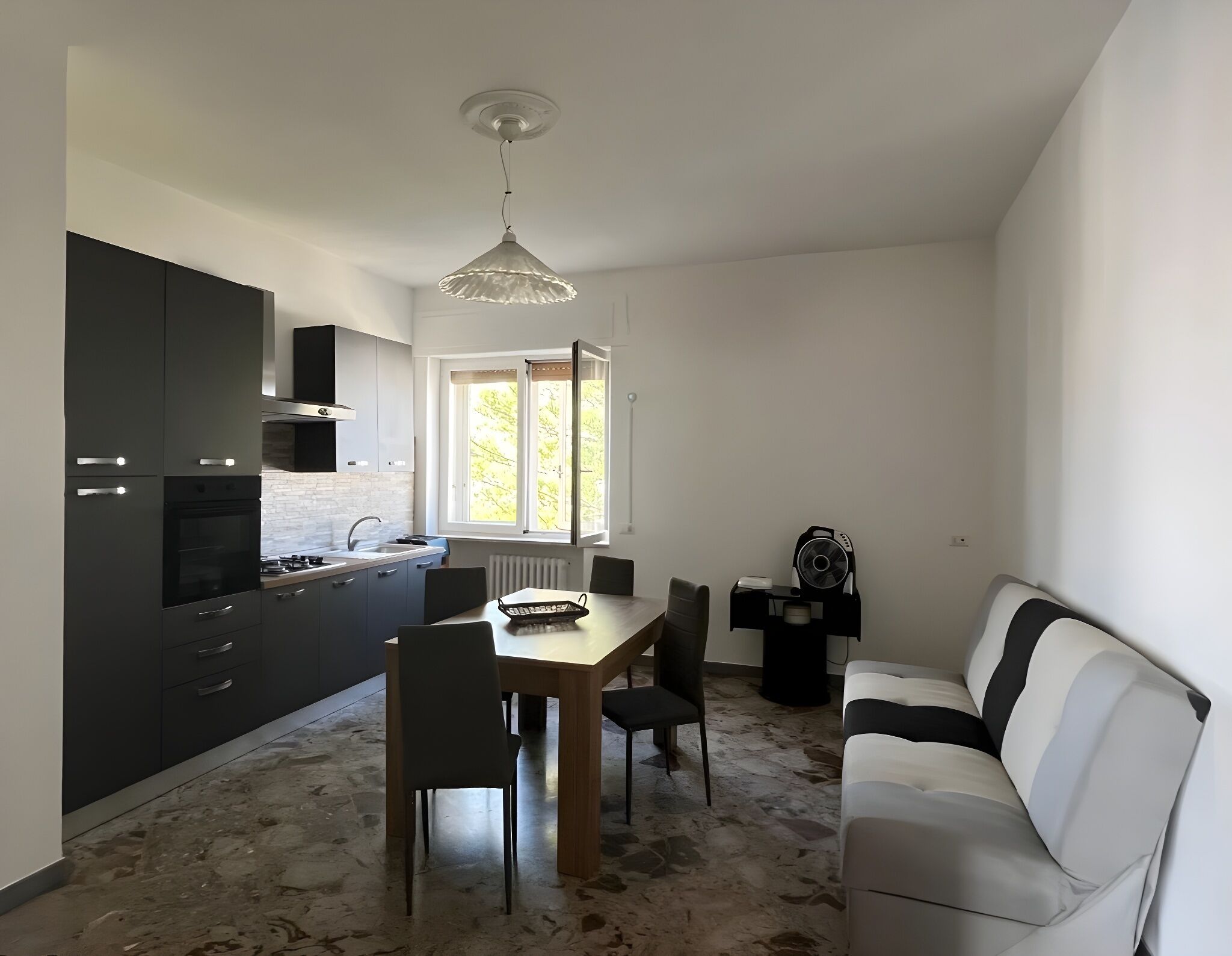 Eine kompakte Küche mit dunklen Schränken, einem Esstisch und Stühlen. Ein weißes Sofa steht an der Wand, und ein Fenster sorgt für natürliches Licht.