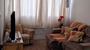 A living room with a sofa, a wooden coffee table, a television, and a ceiling fan. - Ap Próximo ao IME UFRJ e Pão de Açúcar (Rio de Janeiro)