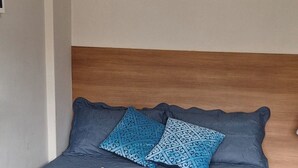 A neatly made bed with a blue bedspread, two patterned pillows, and a rolled white towel. - Ap Próximo ao IME UFRJ e Pão de Açúcar (Rio de Janeiro)