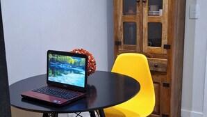 A dining area with a round table, two yellow chairs, a laptop, and a wooden cabinet. - Ap Próximo ao IME UFRJ e Pão de Açúcar (Rio de Janeiro)
