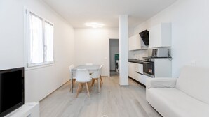 En moderne, minimalistisk stue med et fladskærms-tv, et spiseområde med bord og stole, en hvid sofa og et køkken med mikroovn og ovn.