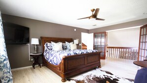 Une chambre avec un lit en bois, un ventilateur de plafond, une télévision et un balcon avec vue.
