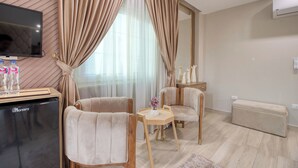 Una sala moderna con televisión de pantalla plana, un minibar, dos sillones, una pequeña mesa de madera y un sofá.