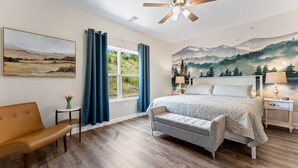 A bedroom with a bed, a bench, a nightstand, a ceiling fan, a window with curtains, and a wall mural. - Luxury Condo / Pool / Game Room / Grill / Pets (Branson)