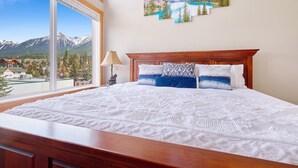 Un grand lit avec une tête de lit en bois, une fenêtre donnant sur les montagnes et une lampe sur la table de chevet.