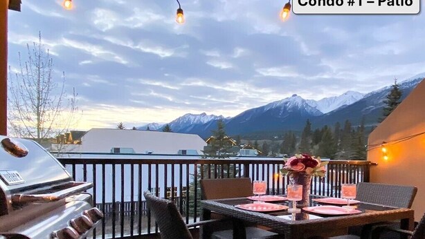 Une terrasse équipée d’un barbecue, d’une table à manger, de chaises et de guirlandes lumineuses.