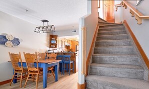 Un comedor con mesa de madera y sillas azules, una cocina con armarios de madera y una escalera con alfombra.