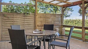 A covered patio with a round table and four wicker chairs, surrounded by a wooden fence and a view of a grassy area. - Awesome home in Tønder with WiFi (Tønder)