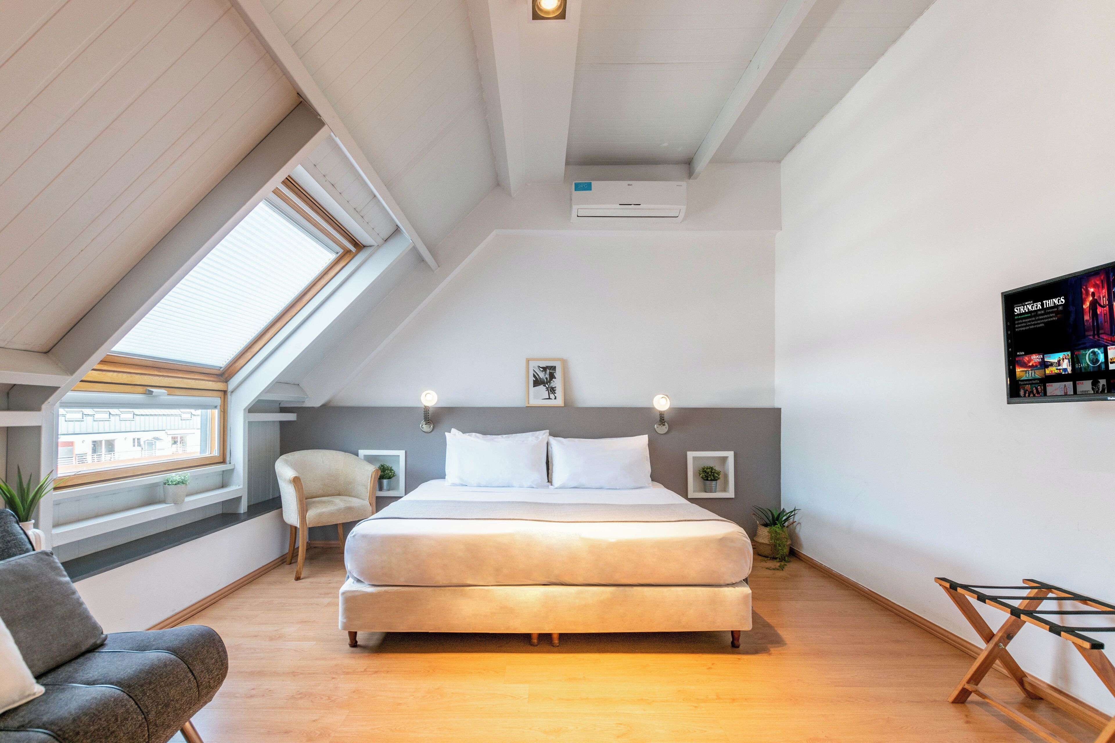 Quarto moderno com cama grande, claraboia, televisão montada e uma pequena planta.