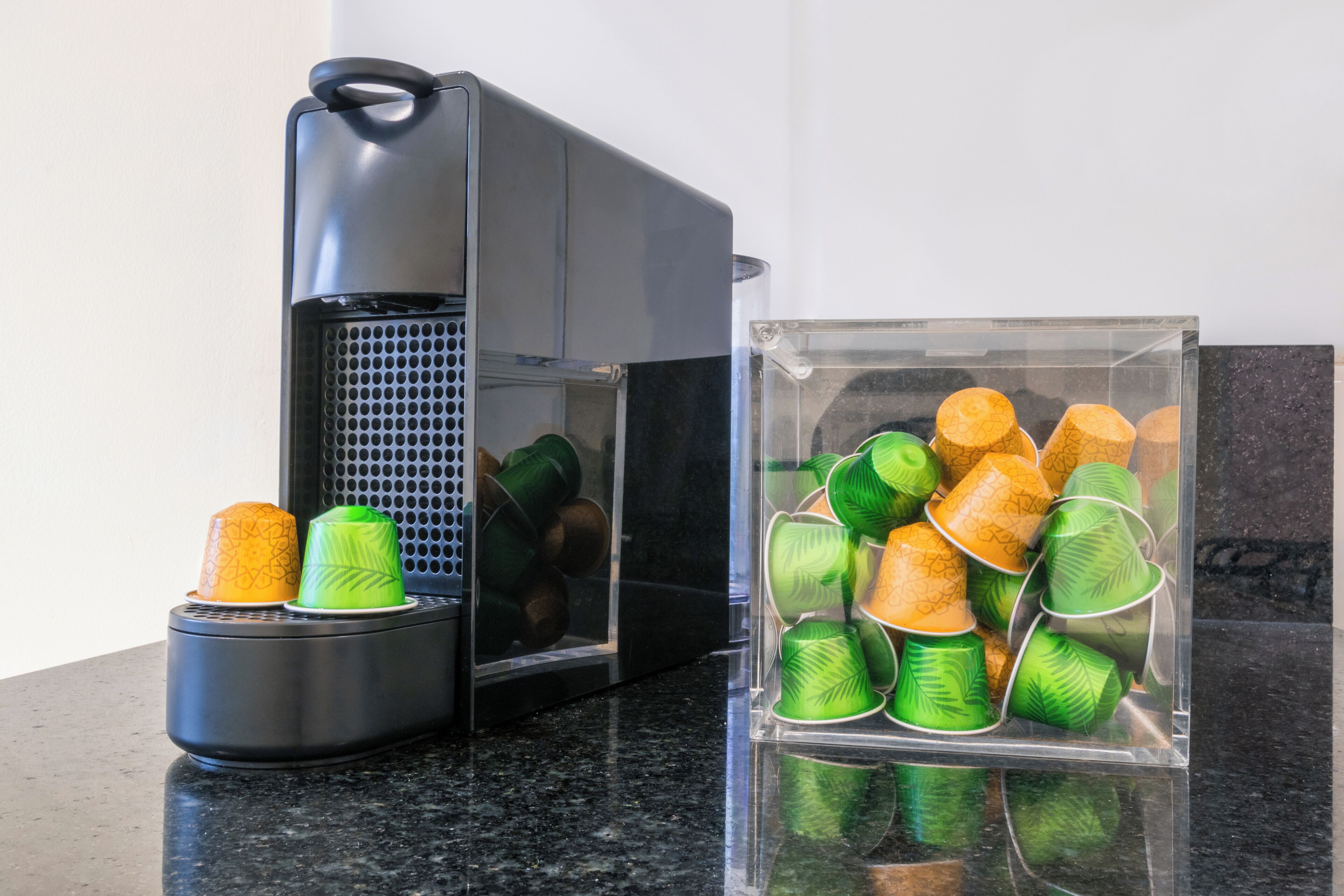 Eine Kaffeemaschine und ein Behälter mit grünen und orangefarbenen Tassen auf einer Arbeitsplatte.