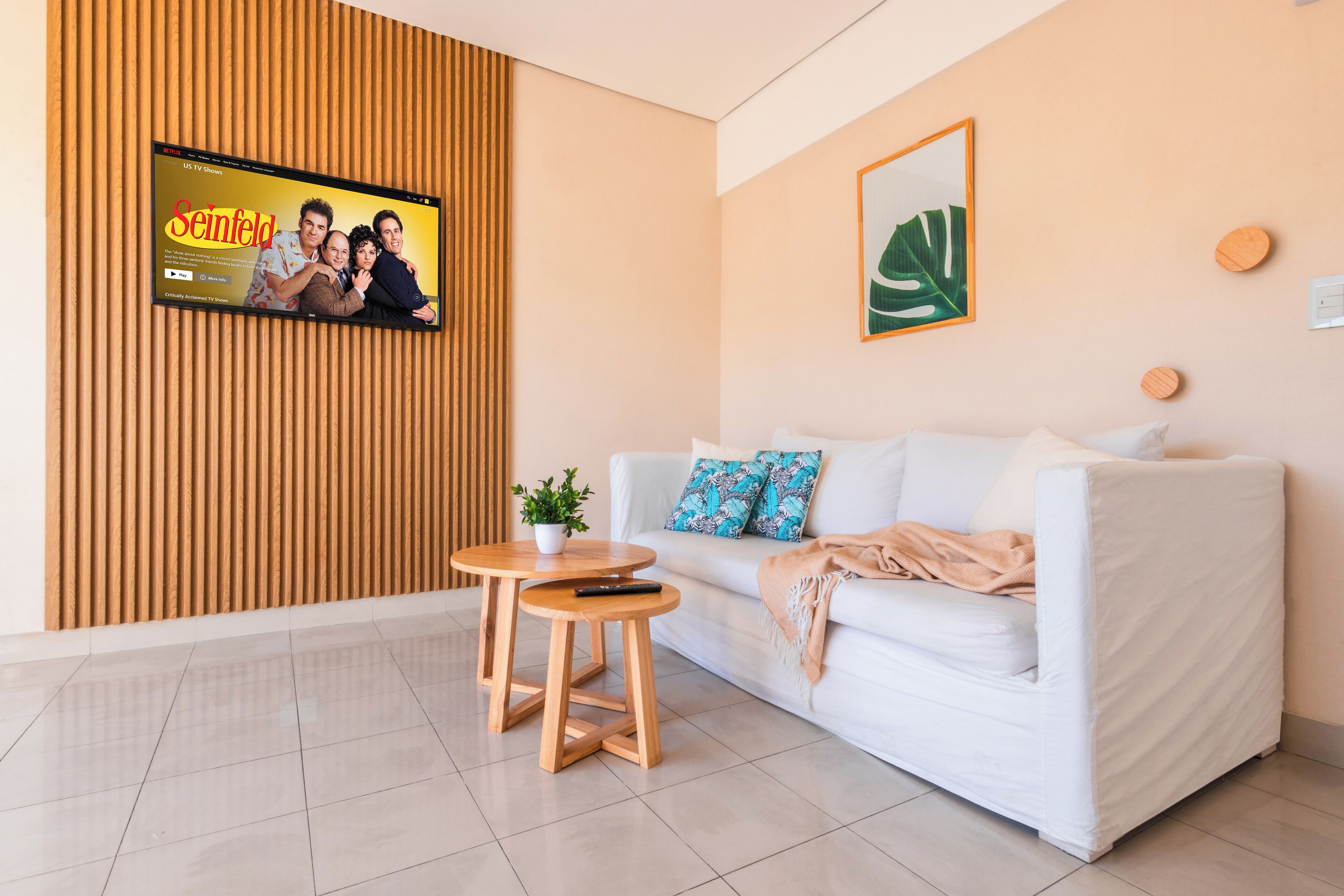 A modern living room with a white sofa, a small wooden table, and a TV mounted on a wooden panel wall.