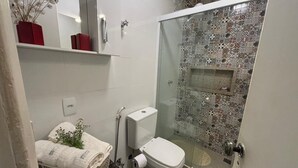 Une petite salle de bain comprenant des toilettes, une cabine de douche en verre et une petite étagère sur laquelle est posé un vase.